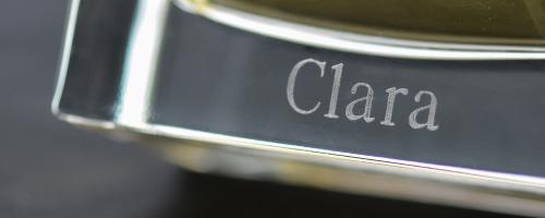 Incisione del nome "Clara" sul fondo di un flacone di profumo in vetro trasparente