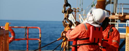 Two operators haul cargo from ship to platform with hook and crane