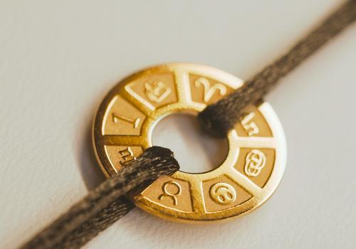 Medaglione gioiello personalizzato in oro con incisione dei segni zodiacali, legato a un braccialetto in cordoncino nero